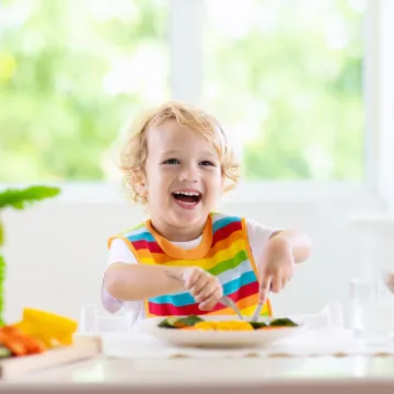 © AdobeStock_276236448 Lachendes Kleinkind beim Essen